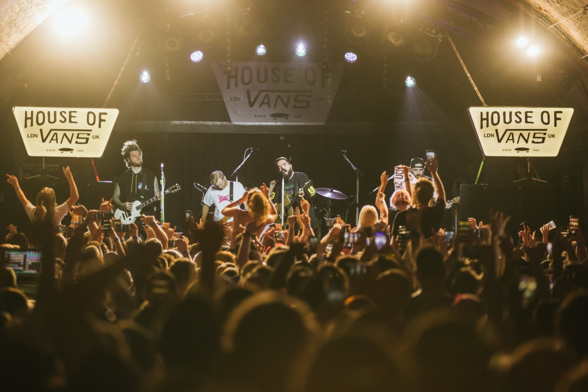 A band plays on a stage in a tunnel, with many spectators in the foreground...