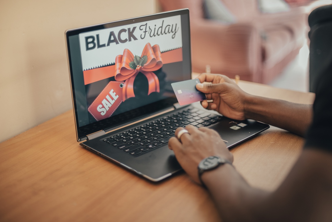 A person is sitting at a laptop. The laptop shows the Black Friday Sale....