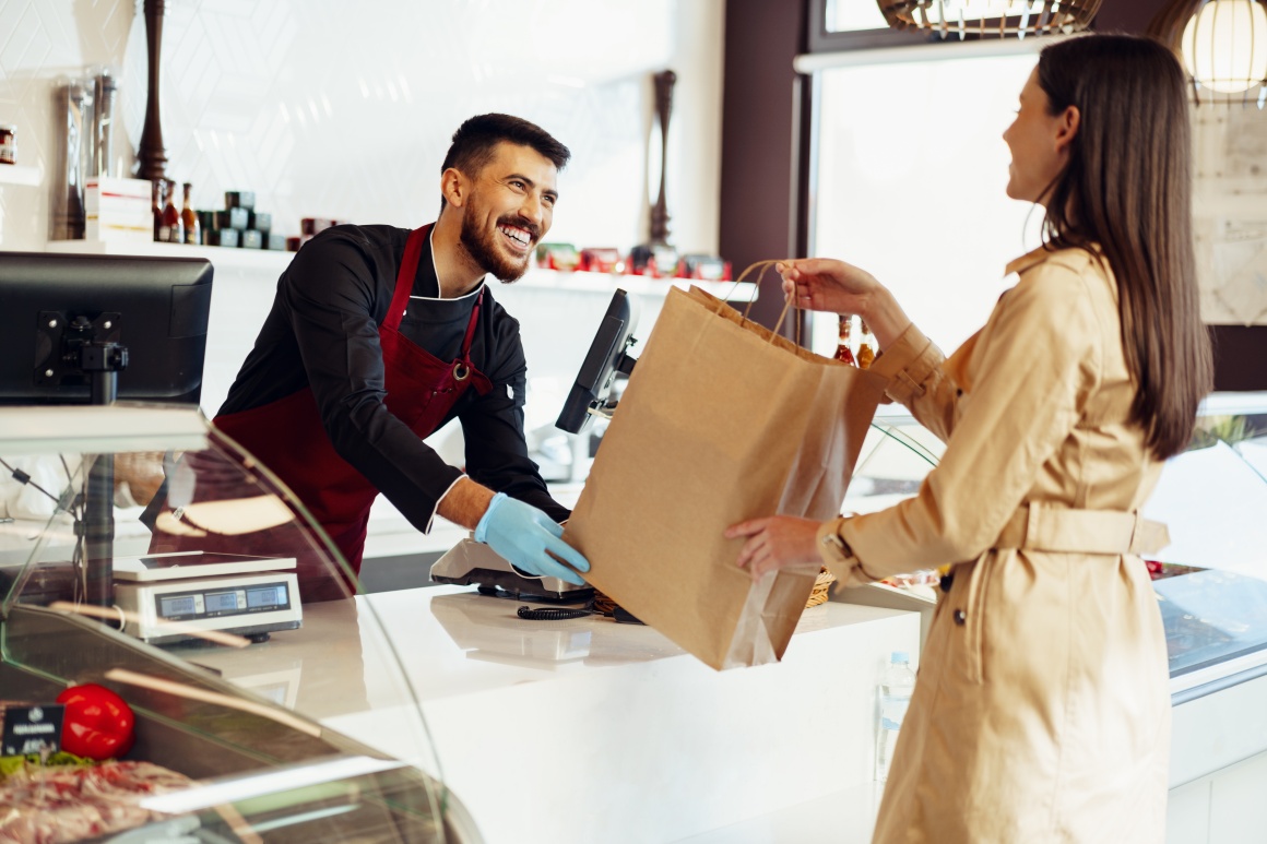 A cashier smilingly hands a customer a bag.