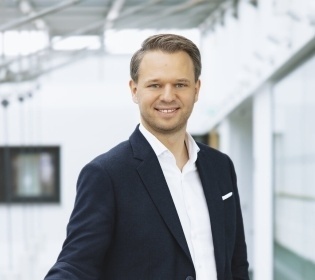 Dr. Philipp Andrée stands smiling in front of a white background....