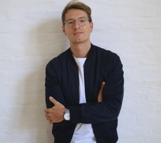 Guillaume Vaslin stands in front of a white wall with his arms folded....