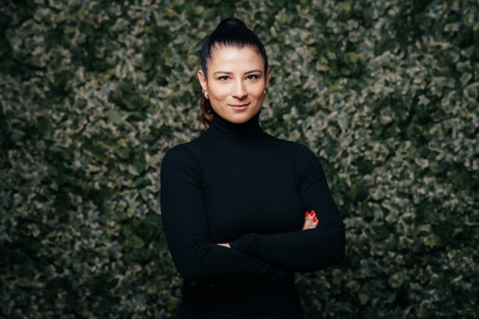 Patricia Grundmann stands in front of a planted wall with her arms folded...