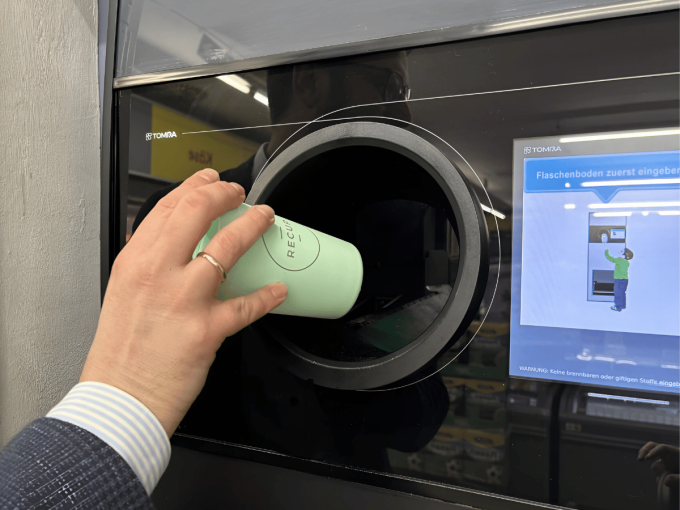 Person inserts a light green reusable cup into the opening of a Tomra reverse...