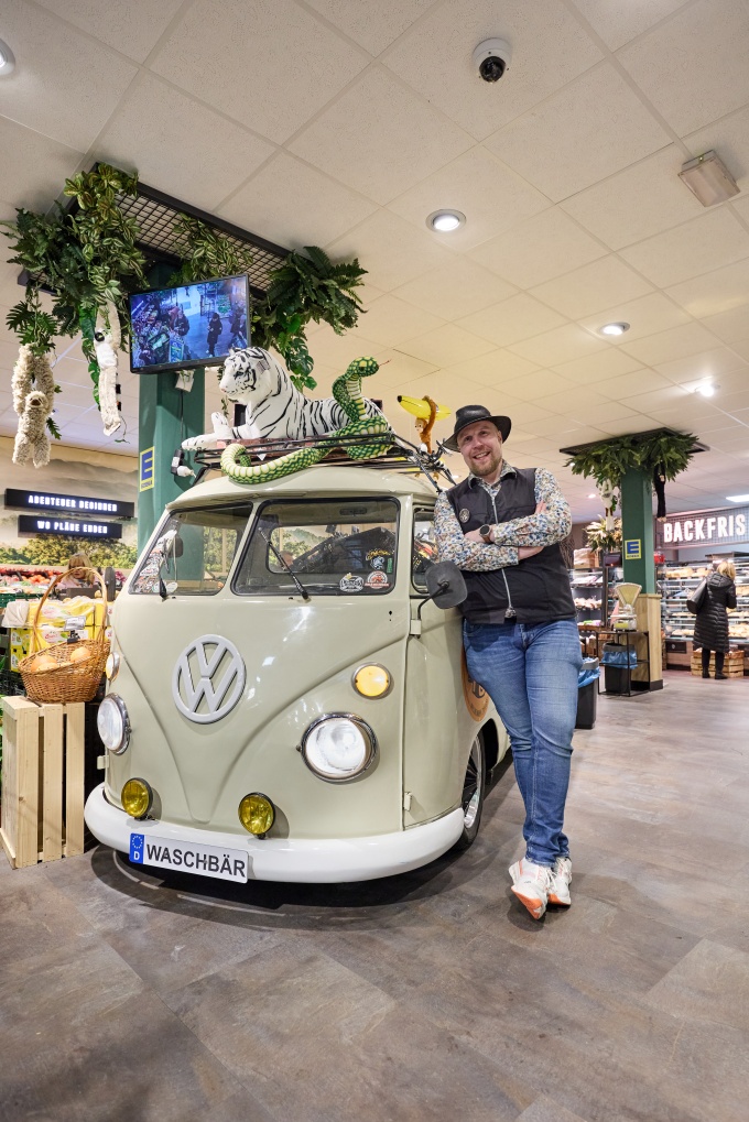 A man wearing a hat is leaning against an old VW bus at a store...