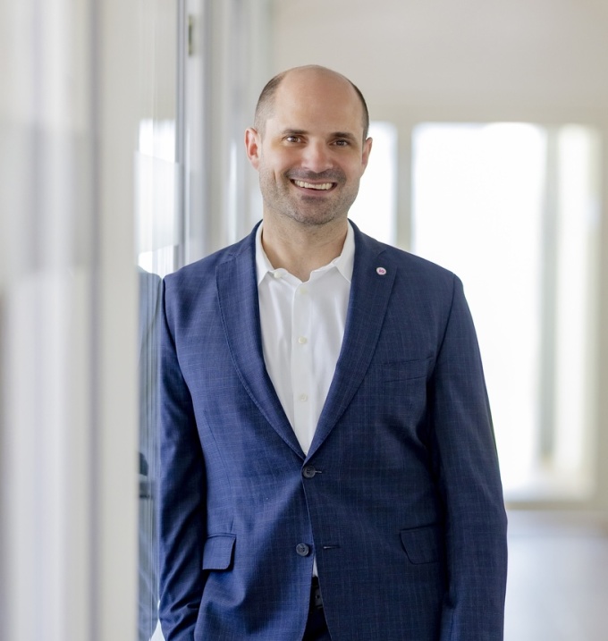A man in a dark blue suit and white shirt smiles at the camera...