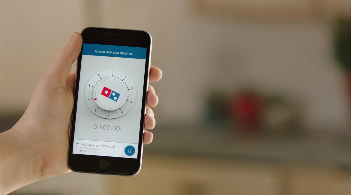 Photo: Hand holding smartphone with Dominos Zero Click Ordering App on display;...