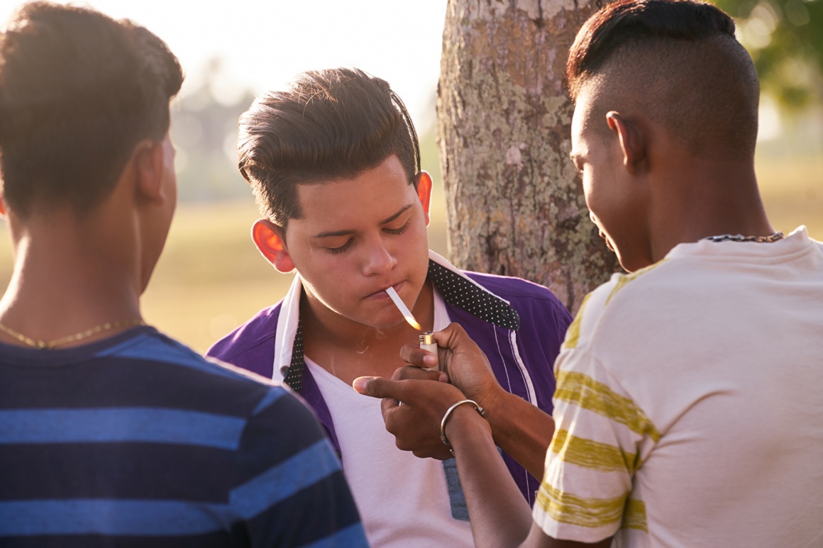 Three boys standing together, one smoking a cigarette; copyright:...