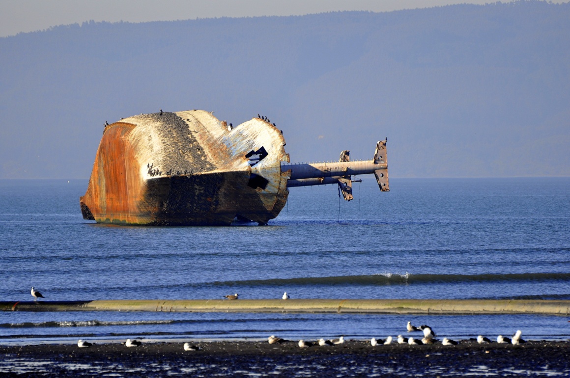 Wrecked ship lying on its side in the sea close to the shore; copyright:...