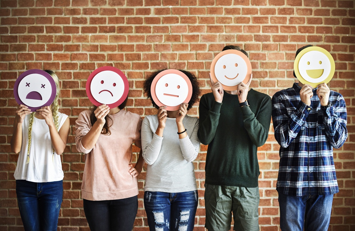 Five people stand in a row and hold smileys in front of their faces....