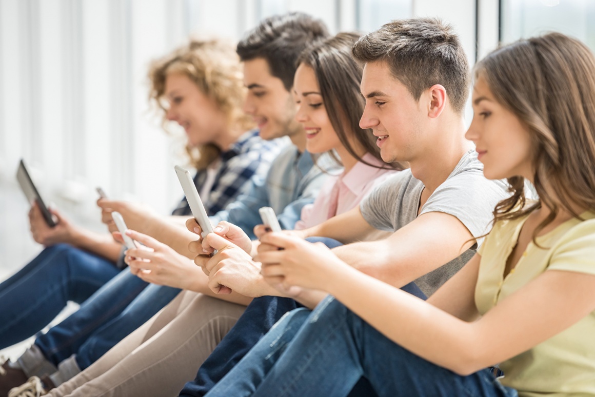 Young people sitting in a row looking at their smartphones; copyright:...