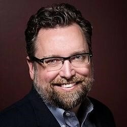 Man with full beard and glasses smiles into the camera...