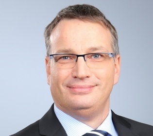 Man in suit, with glasses and blue tie smiles into the camera...
