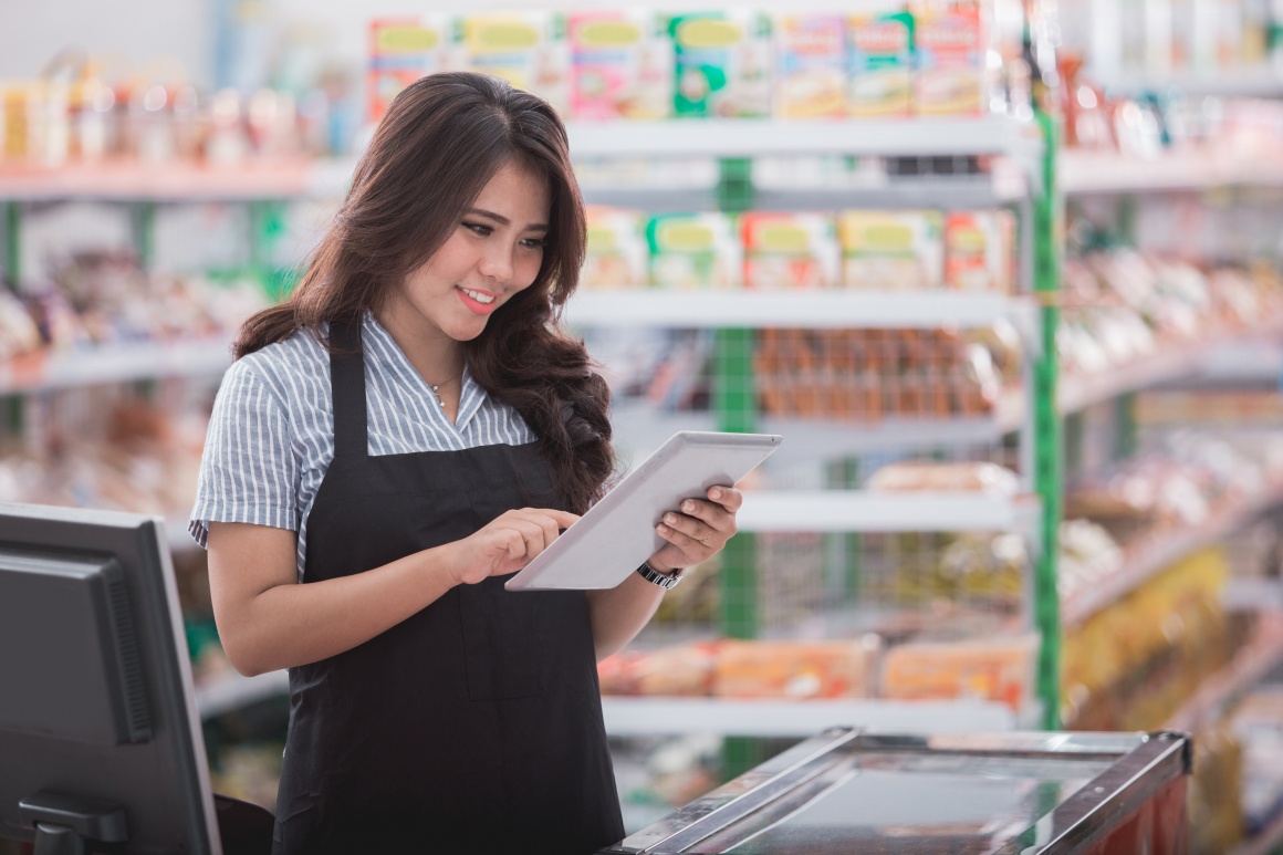 Cashier stands behind the cash register and serves a tablet...