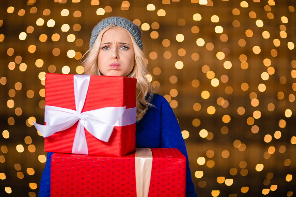 Woman looking unhappy, holding to big wrapped gift boxes under her chin with...
