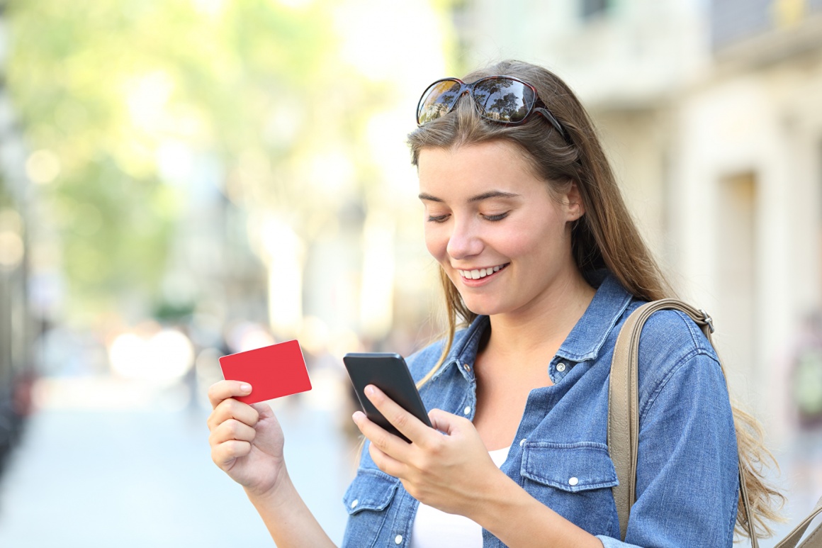 young woman looking at her smartphone while holding a gift card in her hand...