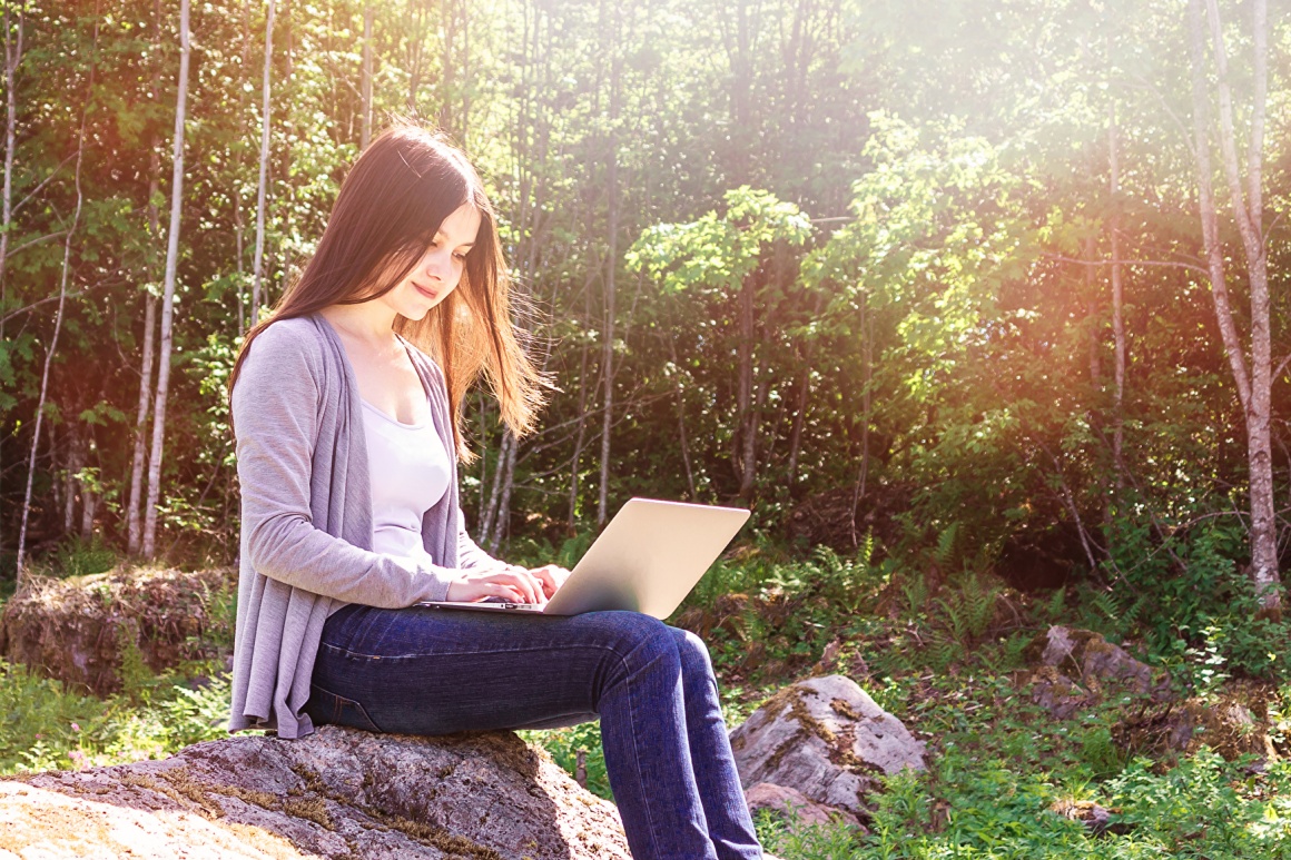 Young woman sitting on a rock and using a computer
