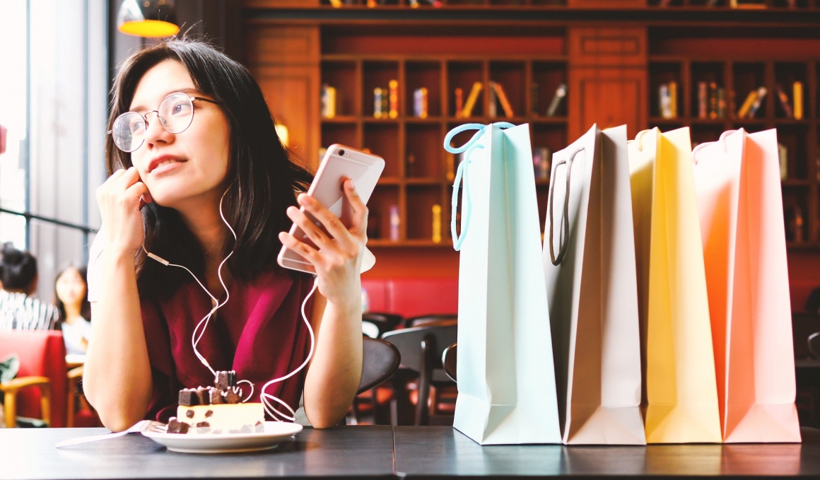 A young woman with headphones and a smartphone sitting at a table. In front of...