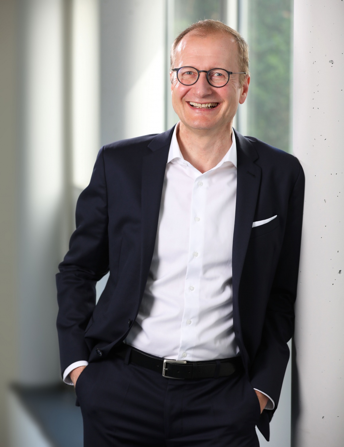 A man in a suit smilingly leans against a wall.