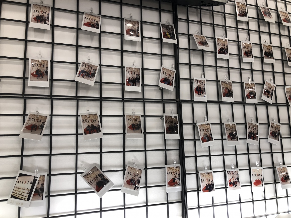 A black grid in front of a white wall with Polaroid photos hanging from it...