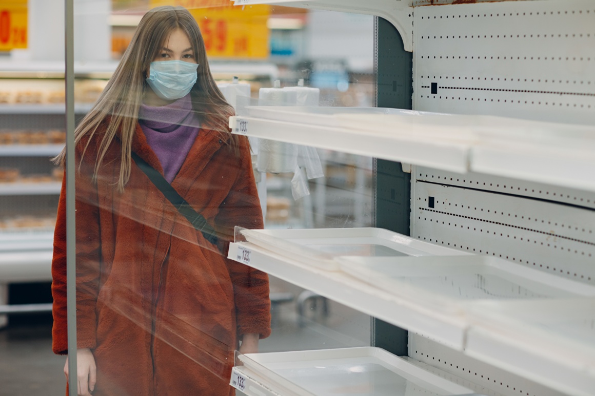 Woman with breathing mask stands in front of empty shelves in the supermarket...