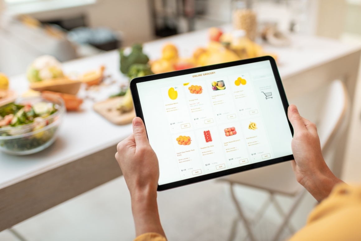 A person is shopping groceries online with a tablet, in front of a table with...