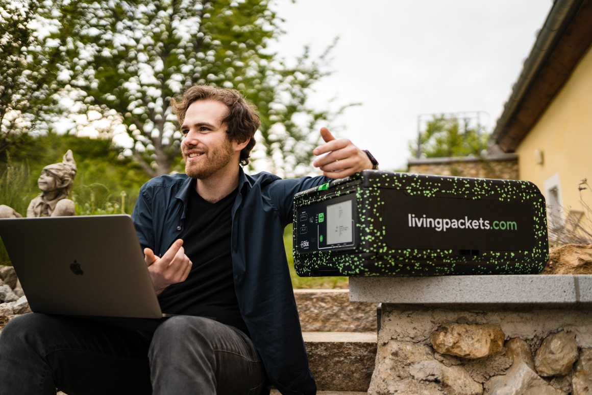 A young man is holding a laptop on his knee, talking and leaning with one hand...