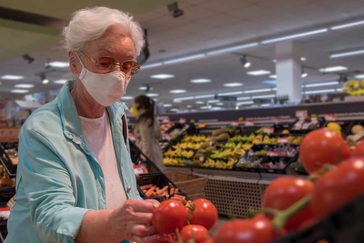 An elderly woman is looking at tomatoes in a supermarket, wearing a face mask...