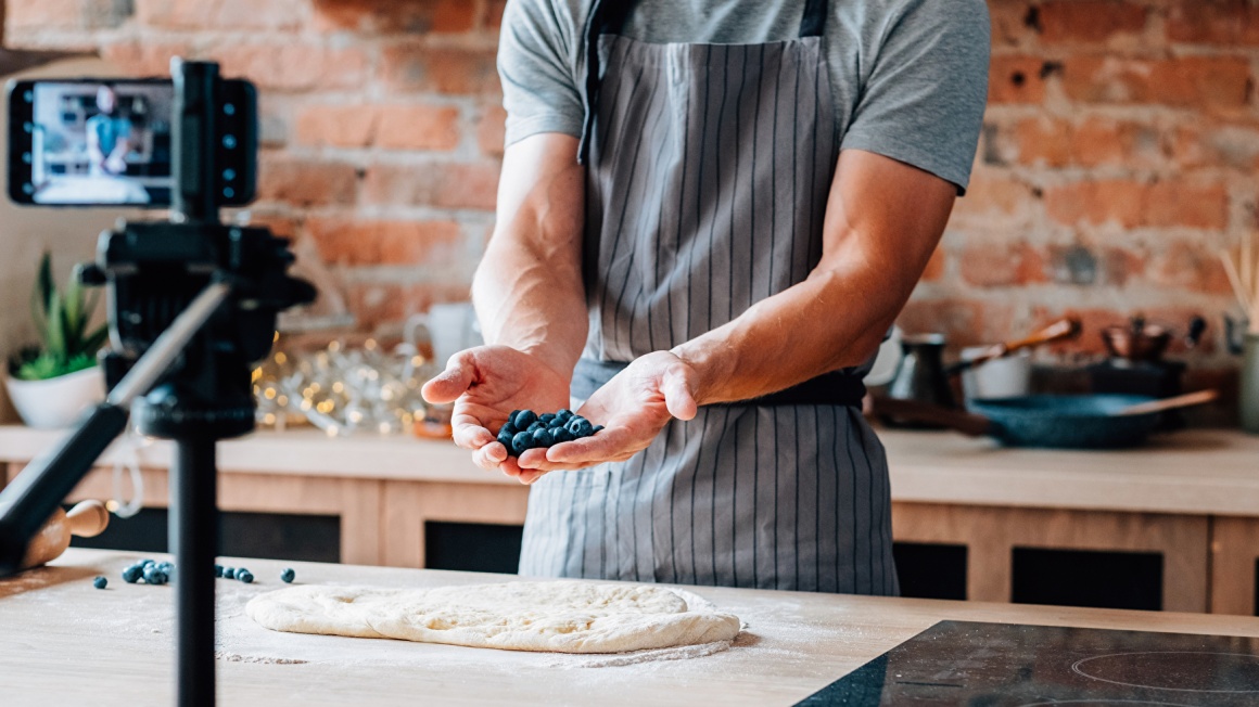 A man in a cooking apron shows a handful of berries to a camera...