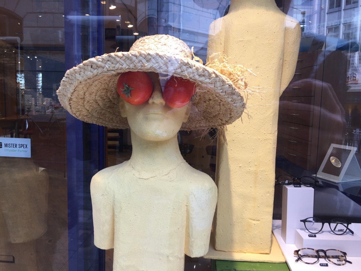 A mannequin with straw hat and tomatoes over its eyes, glasses displayed next...