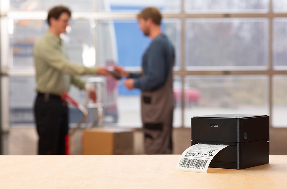 A small printer in the foreground and two people talking to each other in the...