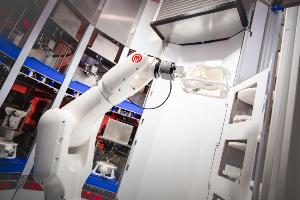 A robotic arm in a machine putting a plastic bowl into a compartment...