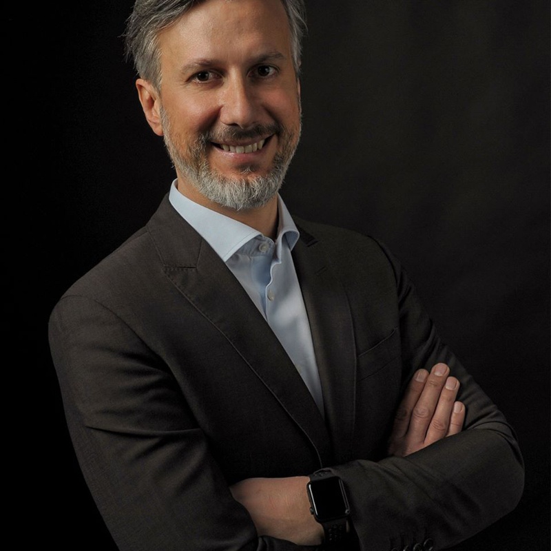 A man in a suit leans against a wall and smiles at the camera...