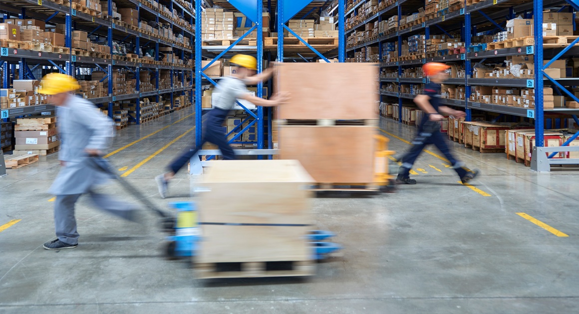 Several workers move boxes on push carts in a warehouse...