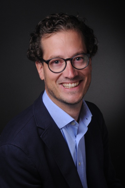 A man with glasses and suit laughs at the camera