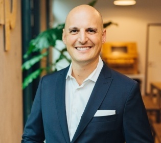 Man in suit without hair folds hands and smiles at camera...