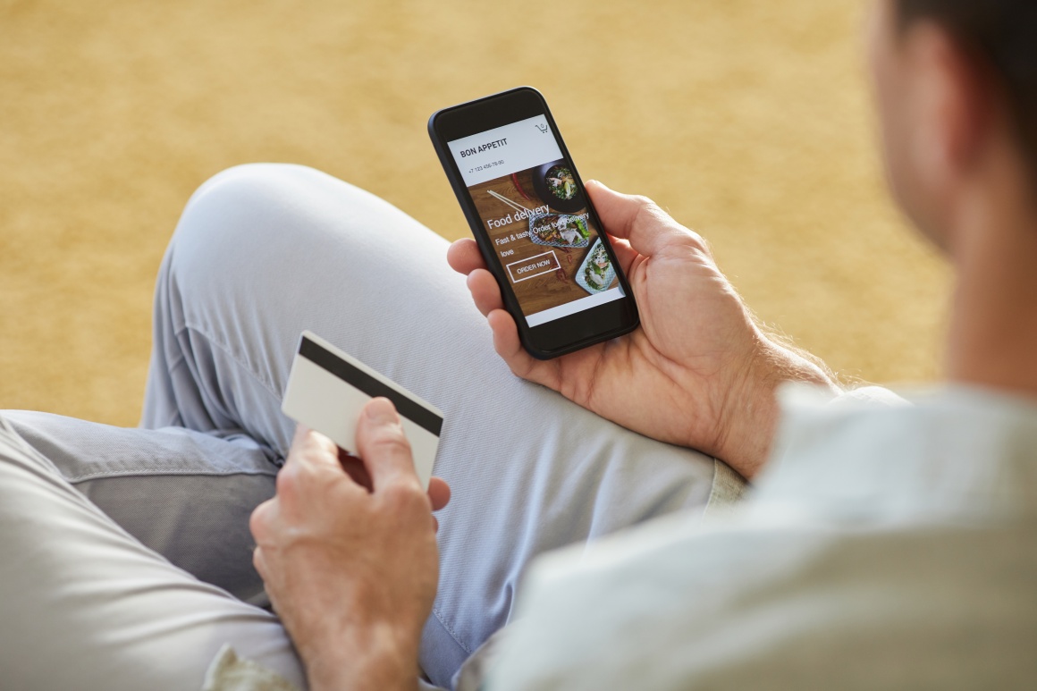 Over the shoulder: man holding smartphone with app open for online ordering....