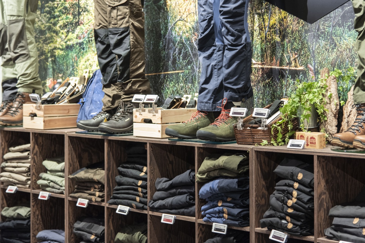 Shelf with pants and hiking boots, marked with digital price tags...