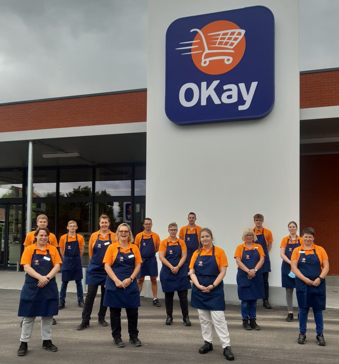 staff wearing orange shirts stand in front of new sustainable local supermarket...
