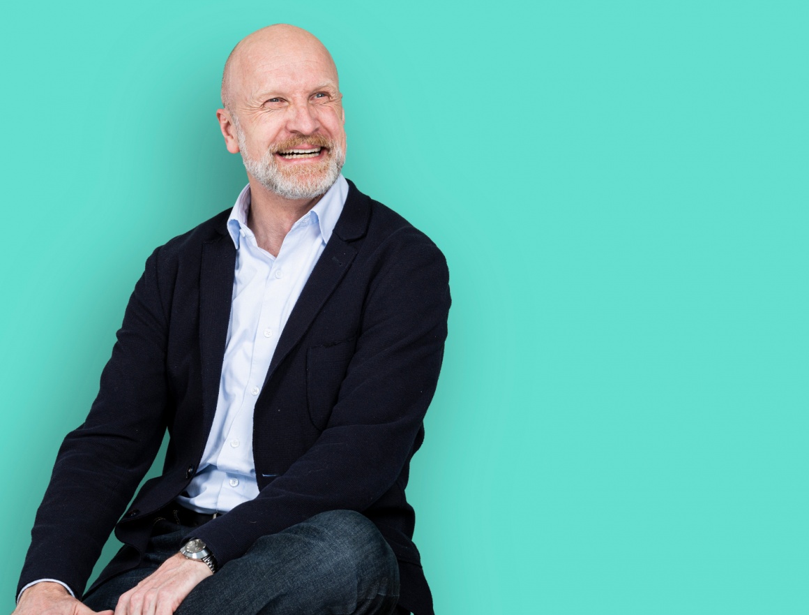 Man in black jacket sits in front of turquoise background...