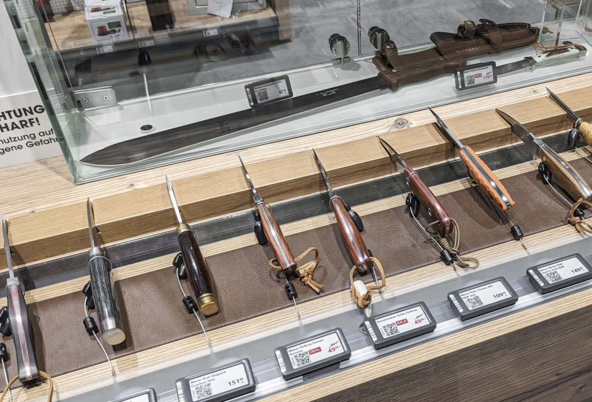 Many knives are in a display side by side with electronic price tags...