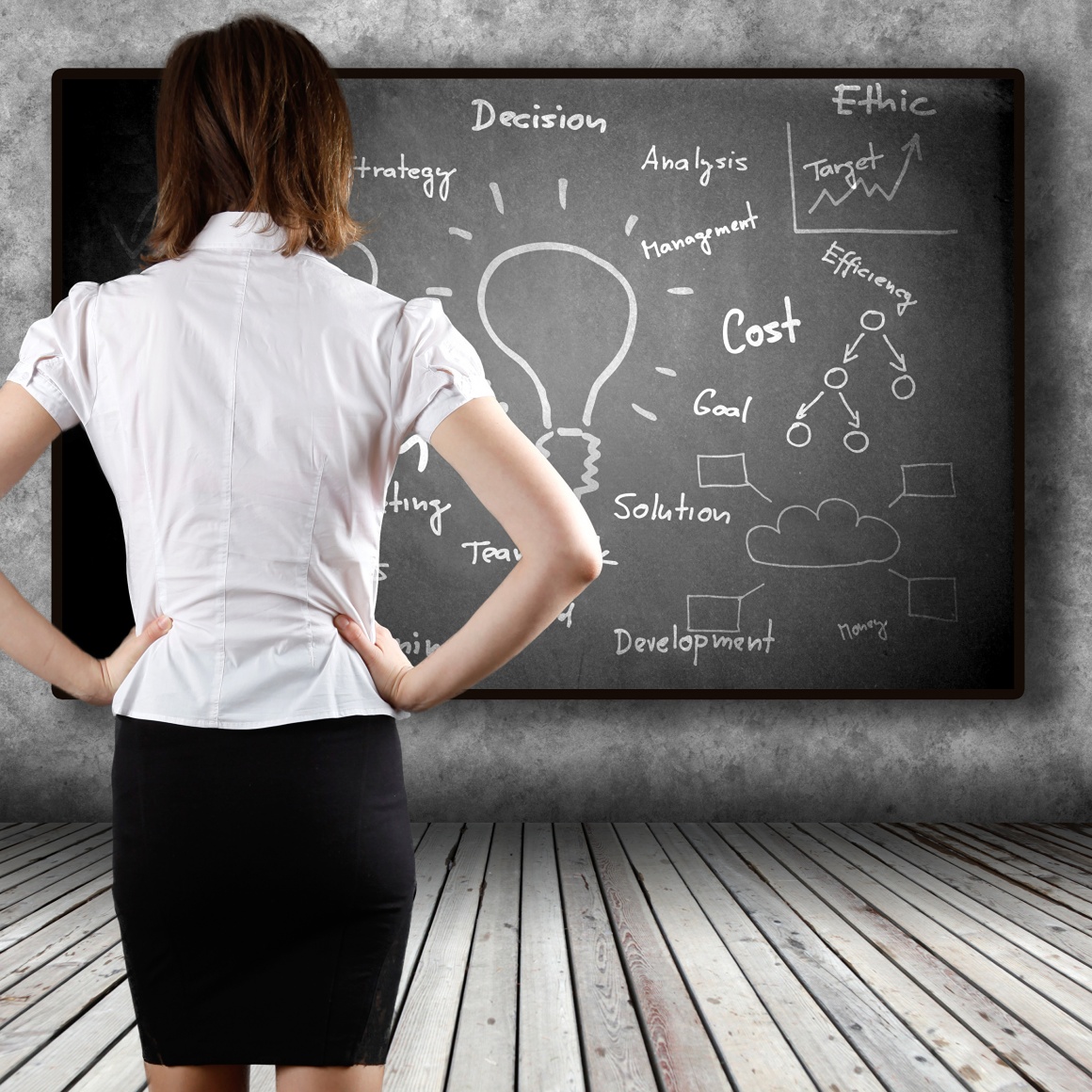 A smartly dressed woman stands in front of a fully written blackboard...