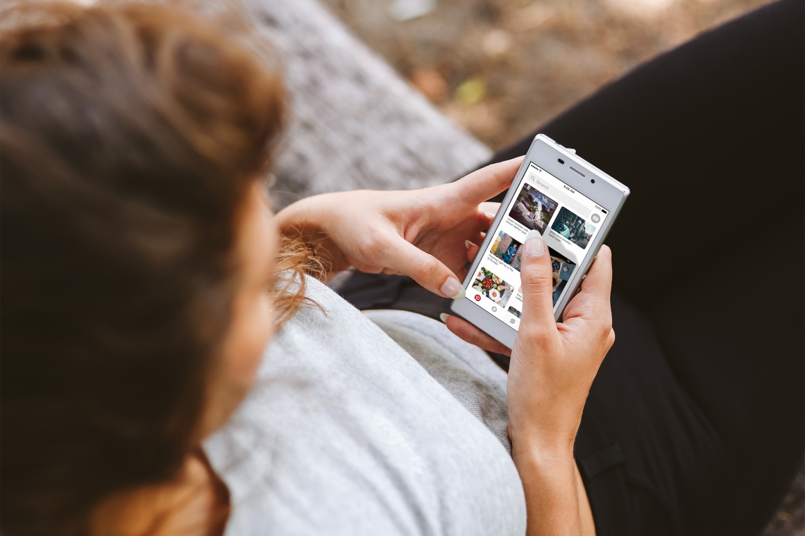 A woman holds her smartphone in her hand and has the Pinterest app open...